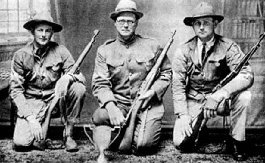 Three World War I era soldiers or rifle team members kneeling in uniform, holding bolt-action rifles, with a trophy placed on the floor in front of them.