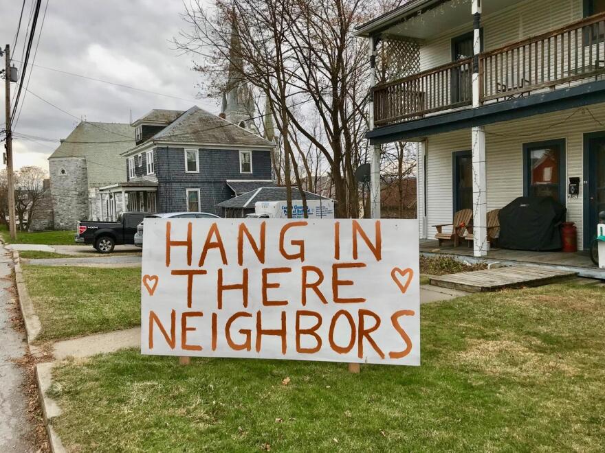 White sign that reads 'Hang In There Neighbors' in red, on a green lawn.