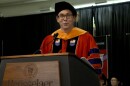 A man in a commencement robe speaks at a podium