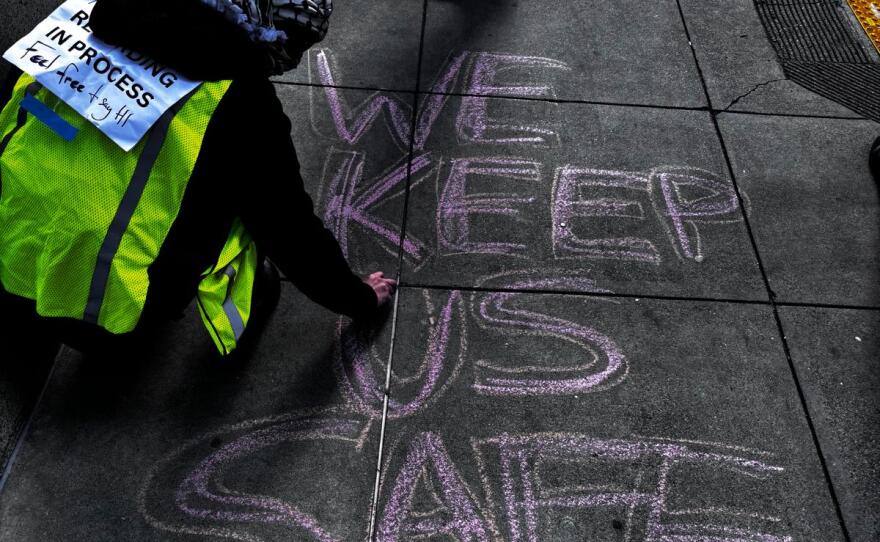 Crouched, Alice draws large letters on the sidewalk with chalk.