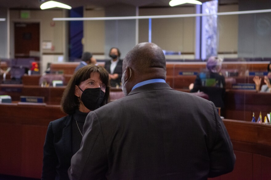 Assemblywoman Robin Titus is wearing a black mask and faces the camera as she speaks to Assembly Speaker Jason Frierson whose back is to the camera. 