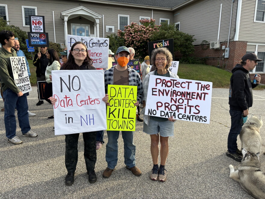 Three people pose holding signs against data centers.