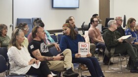 A woman holds a "No Data Centers" sign in the crowd at a city council meeting