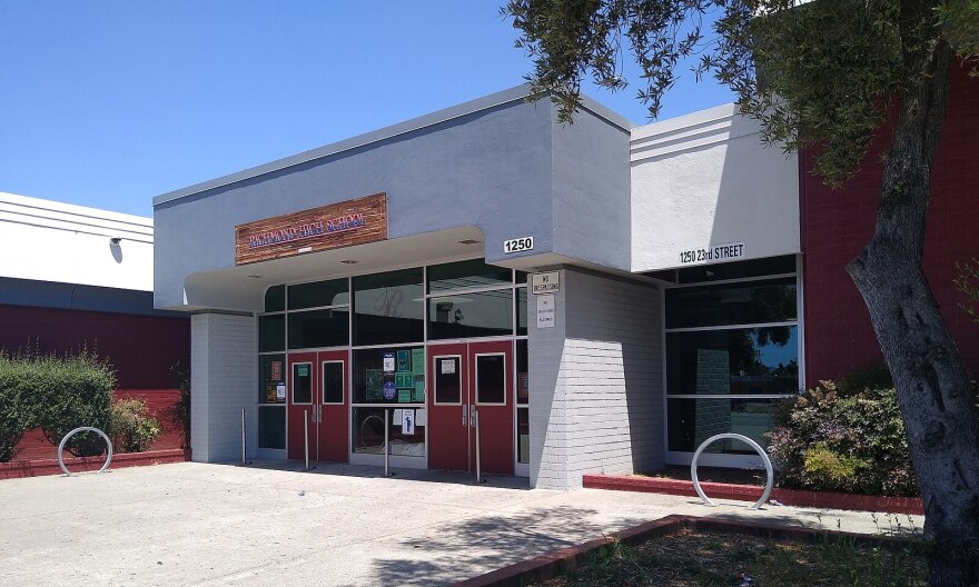 A white building with red doors and a few red walls. A sign on the building reads: Richmond High School. 