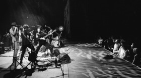  A black-and-white photo of a band performing on stage while a group of fans watches from the front of the stage.
