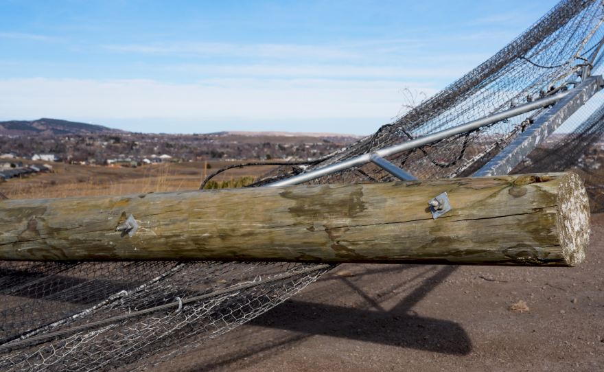 The image shows a large timber pole that was broken in half by the December windstorm. The pole is part of the litter fencing at the Rapid City Landfill.