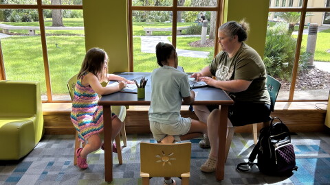 Cheryl Dawson (right), a nurse care coordinator for Partnership for Strong Families, joins a virtual meeting as her daughters, Aria, 8 (left), and Renny, 7, color at the Hawthorne branch of the Alachua County Library District. (Molly Seghi/WUFT News)