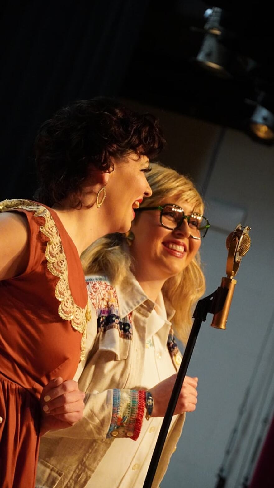 Two woman stand in front of a microphone.