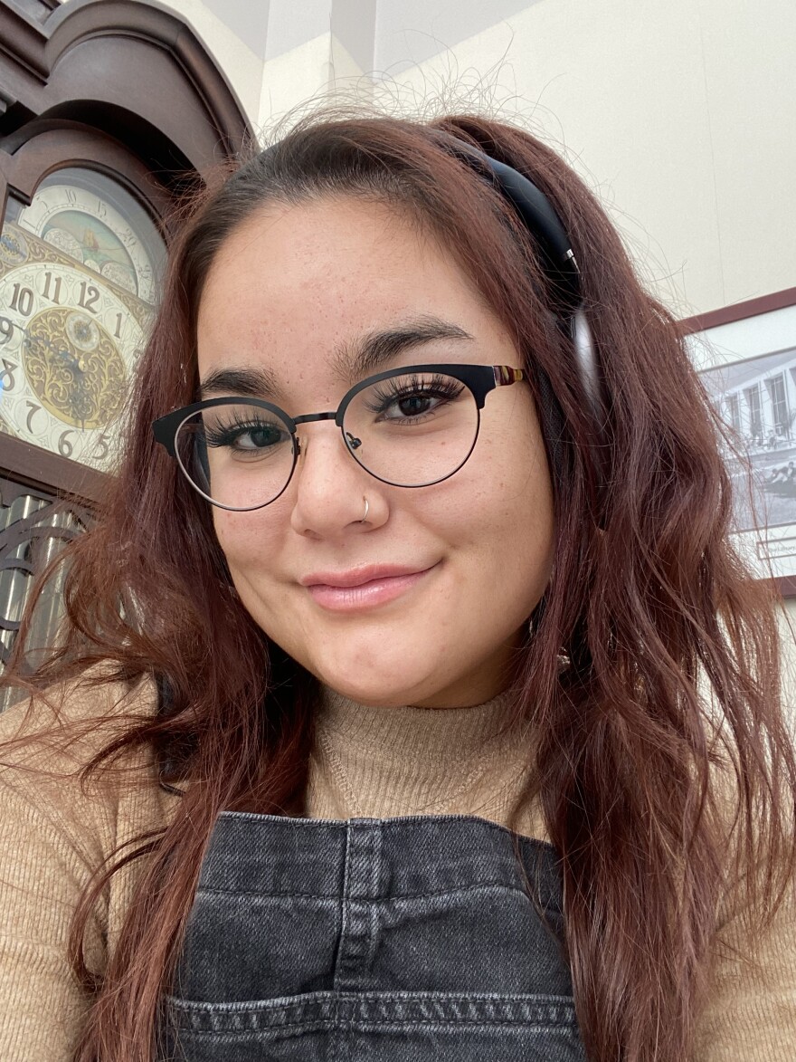 Woman with glasses and dark hair smiling in front of a grandfather clock
