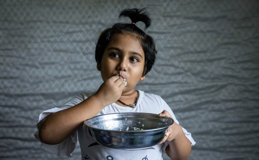 Hosna Ali, 6, eats rice with dried fish at home in Seleyang, Malaysia. Her dad, Mohd Ali, says the family has not been getting enough nutrients during the pandemic.