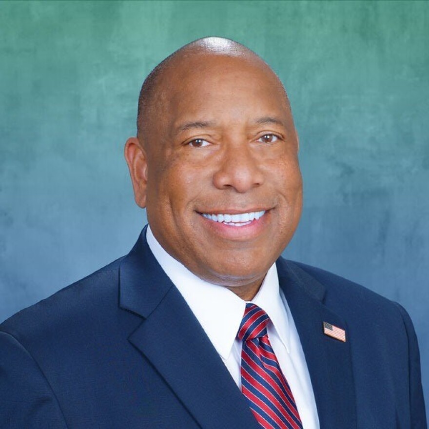 Gubernatorial candidate Semi Bird smiles at the camera in front of a bluish green background