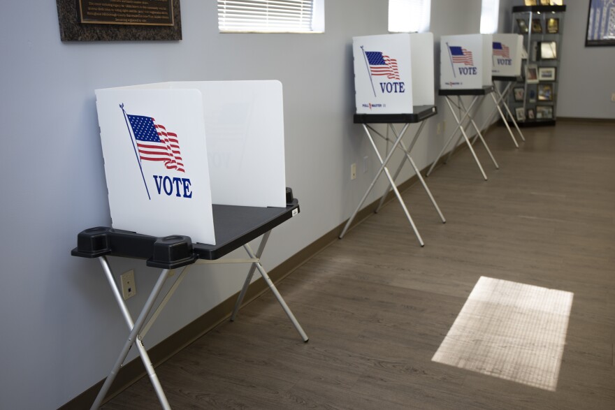 Four voting booths are lined up against a wall. The American flag is on each booth with the word "vote" on them.