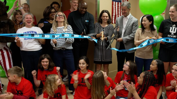 A group of elementary students watch as a ribbon is cut.