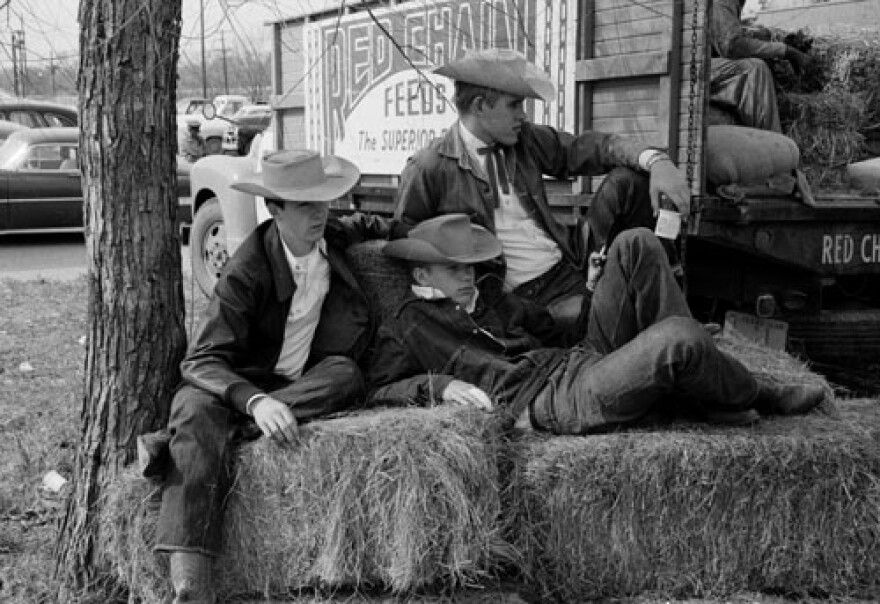  Three cowboys sit on bales of hay at the Austin Livestock Show. 