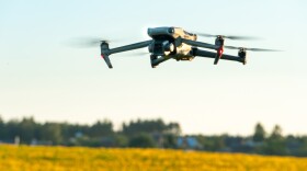 A modern quadcopter drone flies over a field of sunflowers against the sunset. 