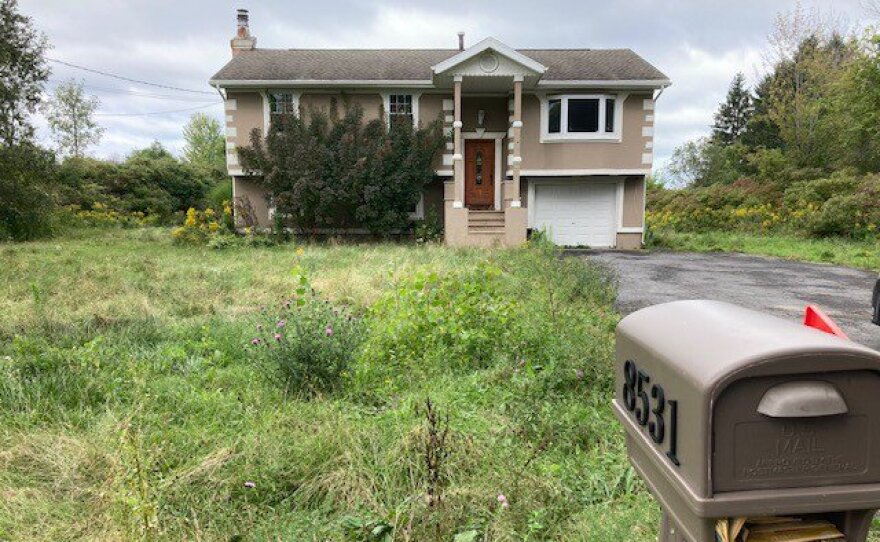 A mail box overflows in front of a house with a grassy green front yard.  