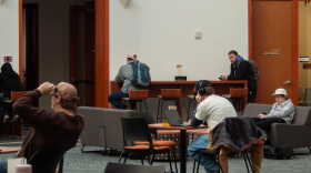 Students sit by themselves at separate tables and couches in a lounge area.