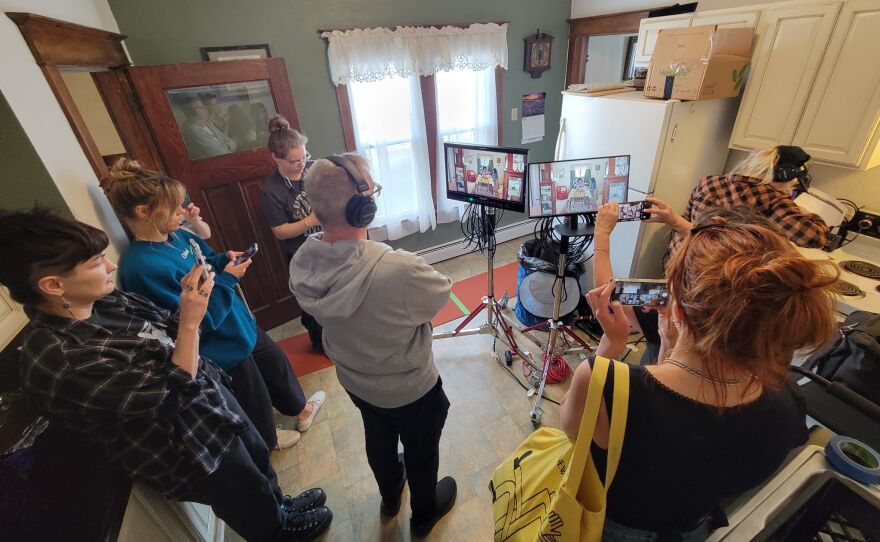 A film crew standing around a couple monitors in a kitchen.