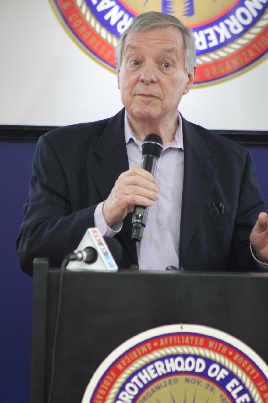 Dick Durbin stands at a podium, speaking and holding a microphone. 