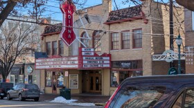 An exterior of a small theater hall with a marquee and cars parked in front.