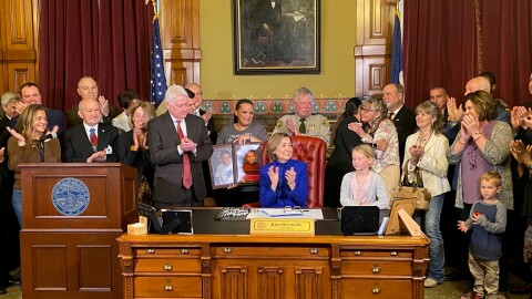 governor kim reynolds claps at her desk surrounded by several people clapping