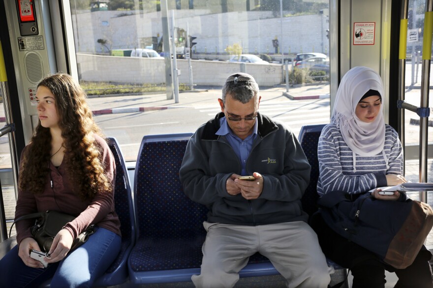David Felber (center) rides the light rail, sitting between Israeli and Palestinian university students. He lives in East Jerusalem and opposed the rail's route through Palestinian neighborhoods, but is now a regular rider.