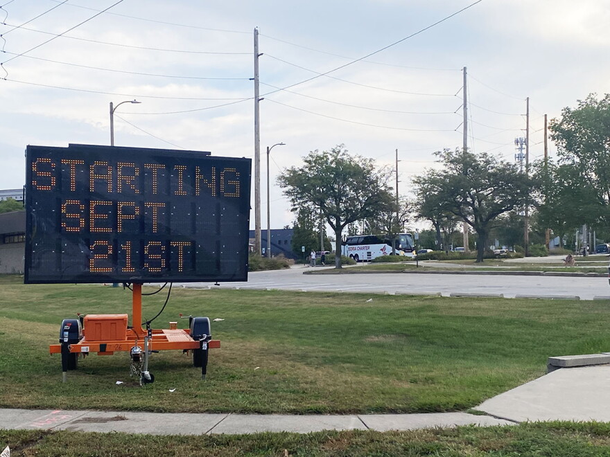 A large electronic sign on wheels placed in a grassy area next to a parking lot. The sign reads 'Starting Sept. 21st.' 