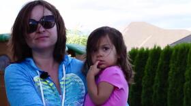 A woman in a blue shirt holds a little girl in a pink shirt