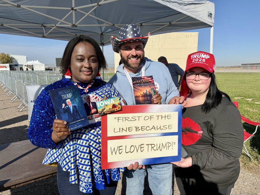 A photo of three people holding a sign that says "First of the Line Because We Love Trump!"
