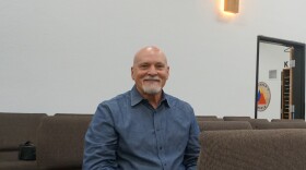 A bald man with a white beard sits in a pew.