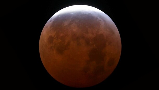 A moon during a lunar eclipse; most of the surface shadowed and red