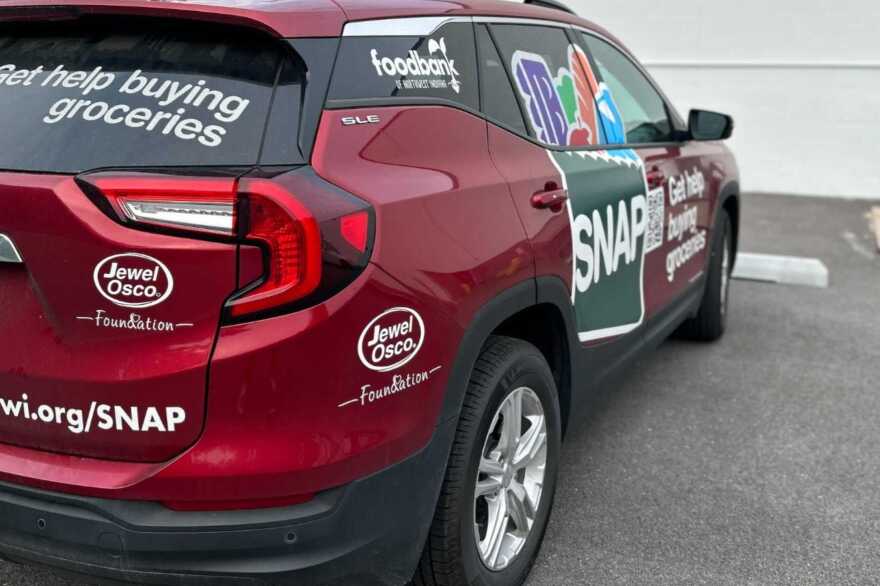  A SNAP vehicle with decals depicting groceries and the SNAP logo is parked in a lot.