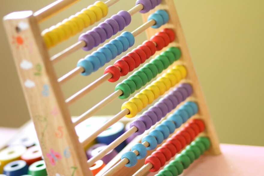 A multicolored wooden abacus sits on a desk in a brightly lit room.