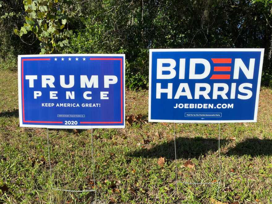 Signs that read TRUMP PENCE and BIDEN HARRIS sit next to each other in a patch of grass
