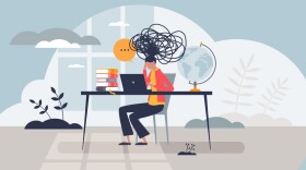 An illustration of a woman sitting at a desk in front of a laptop with scribbles above her head signifying psychological burnout and stress. 