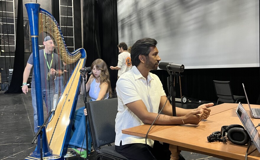 Podcaster and musician Hrishikesh Hirway of Song Exploder is being interviewed by Monte and Kaliis while musician Mikaela Davis tunes her harp.