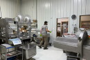 Ryan Freman is speaking to Trey Freman in their processing facility. There are several different processing machines arond.