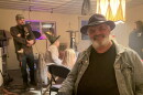 A man with a beard and hat smiling at camera. Behind him a woman in a witch hat and a couple kids