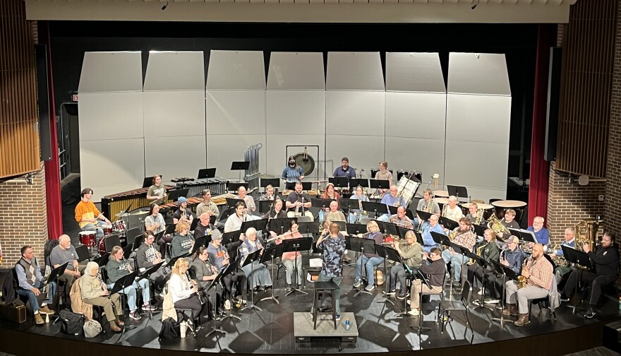 A symphonic band on stage featuring brass, woodwind, and percussion instruments.