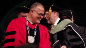 Montgomery, in red and black robe and wearing a medal, leans in to talk to Dunn, in black robe
