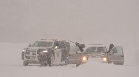 A car is stuck in and covered with snow. A California Highway Patrol vehicle is parked next to it.