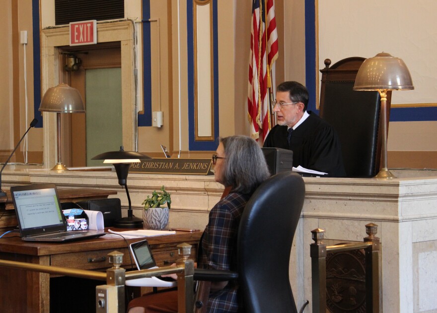 judge sits at his bench, court staffer in the foreground