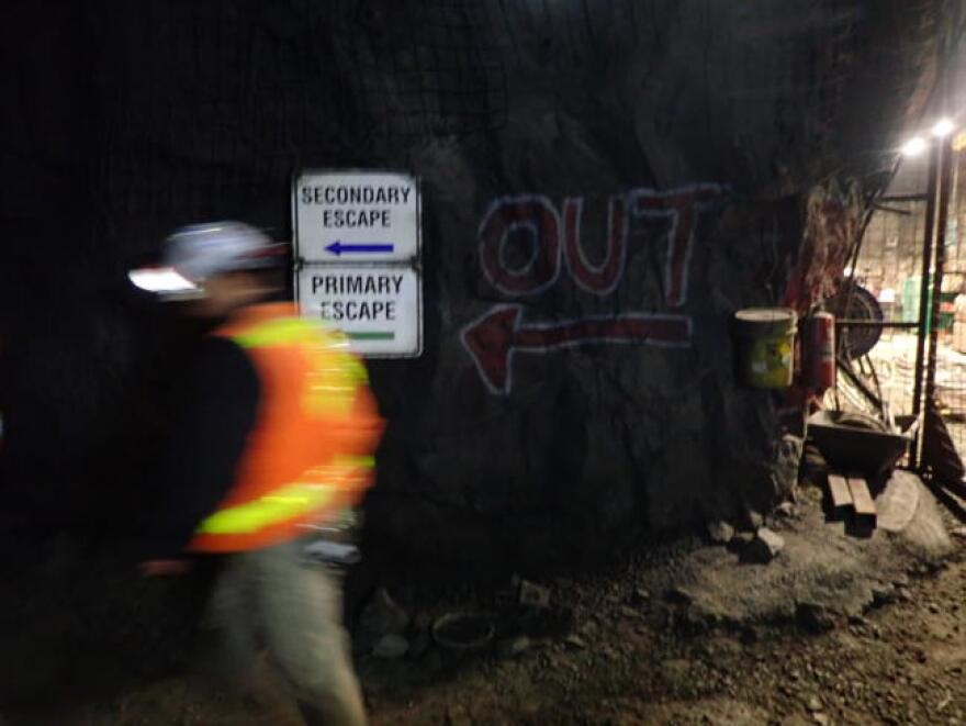 A man in an orange vest walking past exit signs in a mine