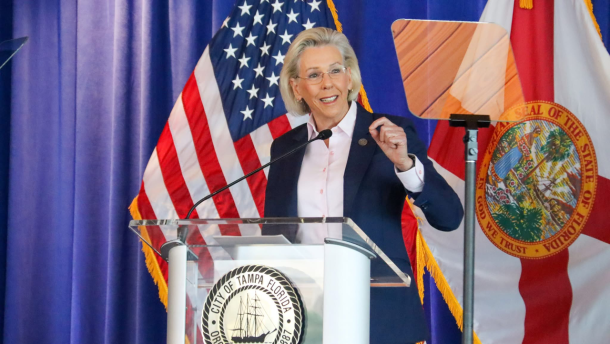 A woman standing in front of a podium speaking with the Florida flag in the background