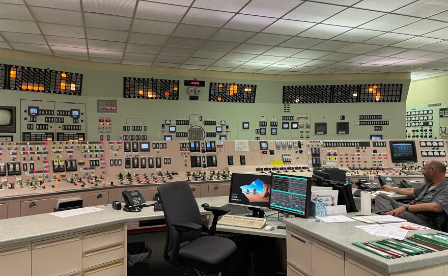 The control room at the Palisades nuclear plant. In the foreground are desks with computer monitors. Behind, a wall of switches and meters.