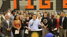 Gov. Bob Ferguson stands with students, teachers and administrators in front of a podium, inside the Lewis & Clark gymnasium. 