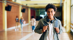 Happy African American high school student standing in hallway and looking at camera.