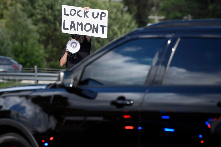 Protestor holds sign that reads "Lock Up Lamont"