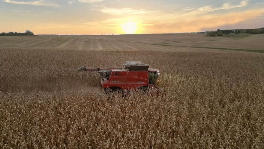 The sun sets over a combine plowing through a field in Illinois