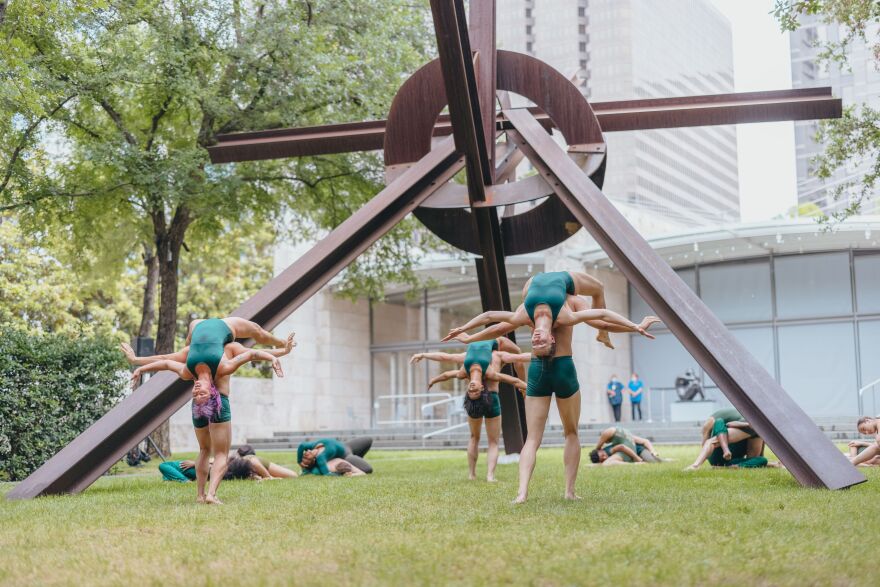 Professional dancers perform under a large-scale outdoor sculpture